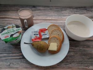 Zdjęcie przedstawia Dietę podstawową: Płatki pszenne na mleku Chleb mieszany pszenno-żytni Masło extra Dżem Serek wiejski ziarnisty Kakao Gruszka